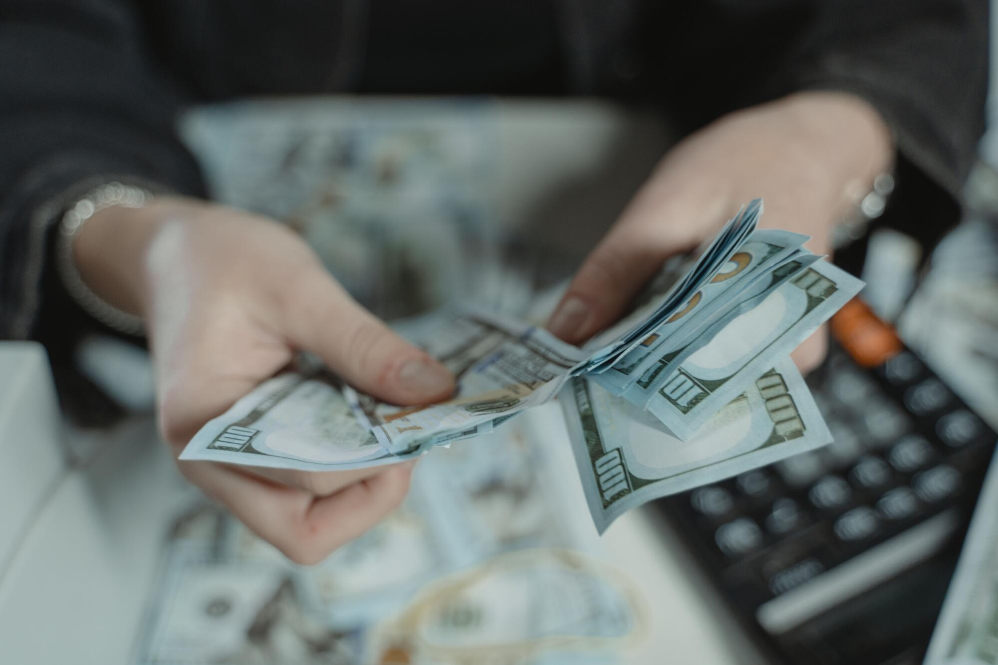 A woman sits at a table counting cash from a short-term cash advance, with a calculator on the table.