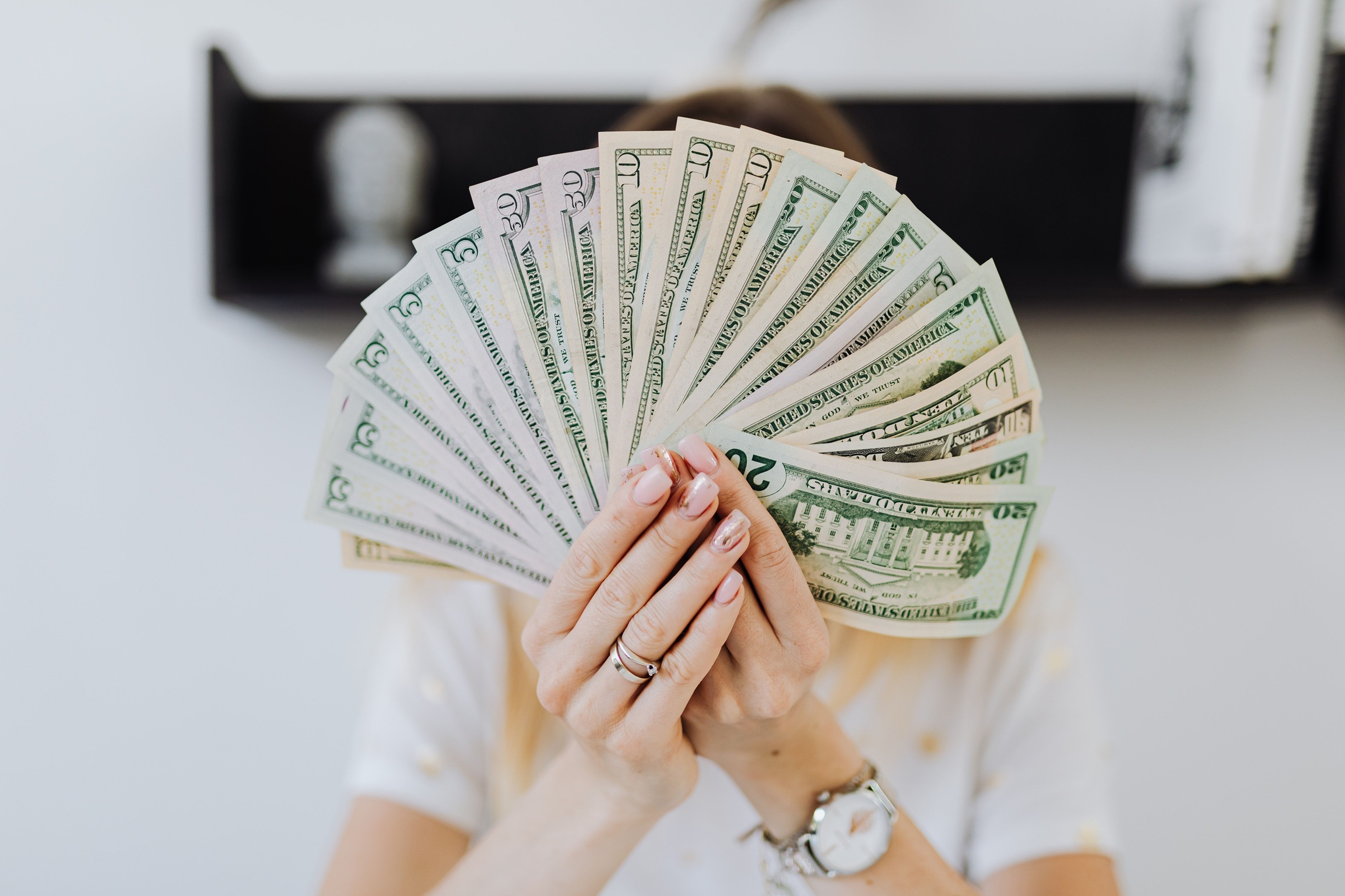 A woman holding cash in both hands fanned out and hiding her face, representing easy payday advance loans