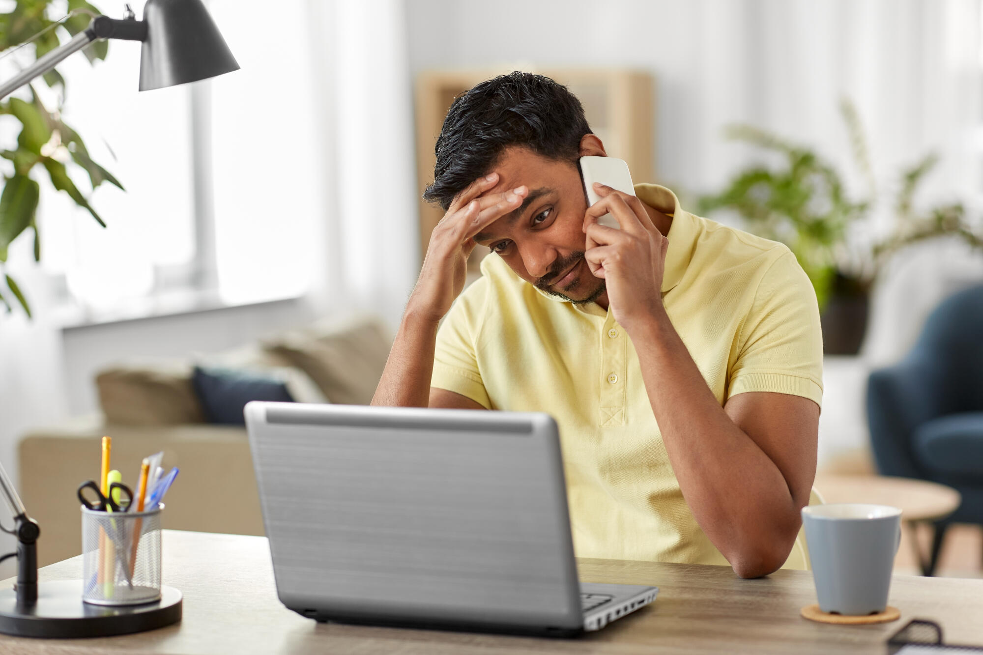 Stressed businessman sitting at a table while speaking on the phone and looking at a computer researching fast loans.