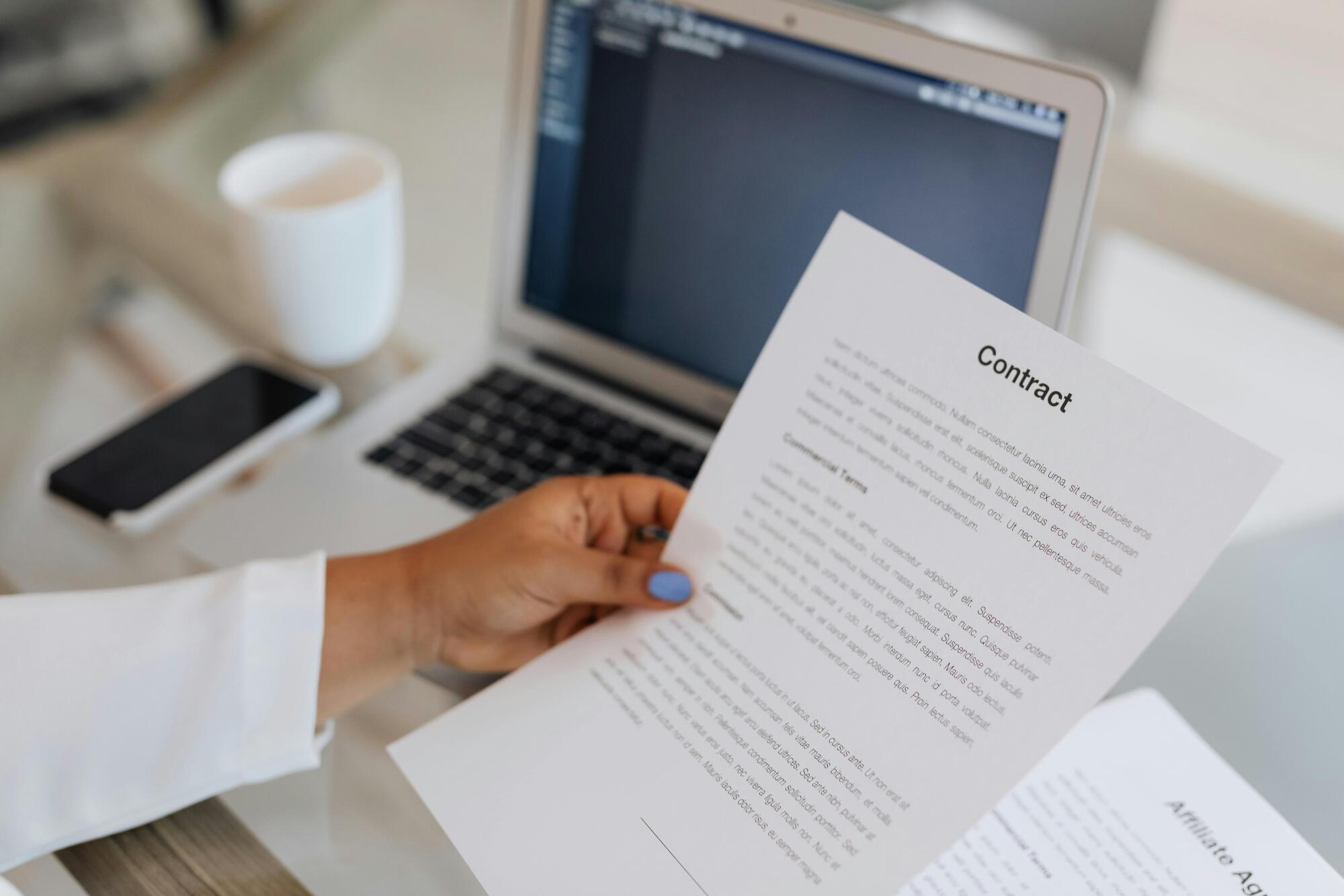 Hand holding a piece of paper, with a laptop in the background showcasing an individual reviewing information on loan renewal.